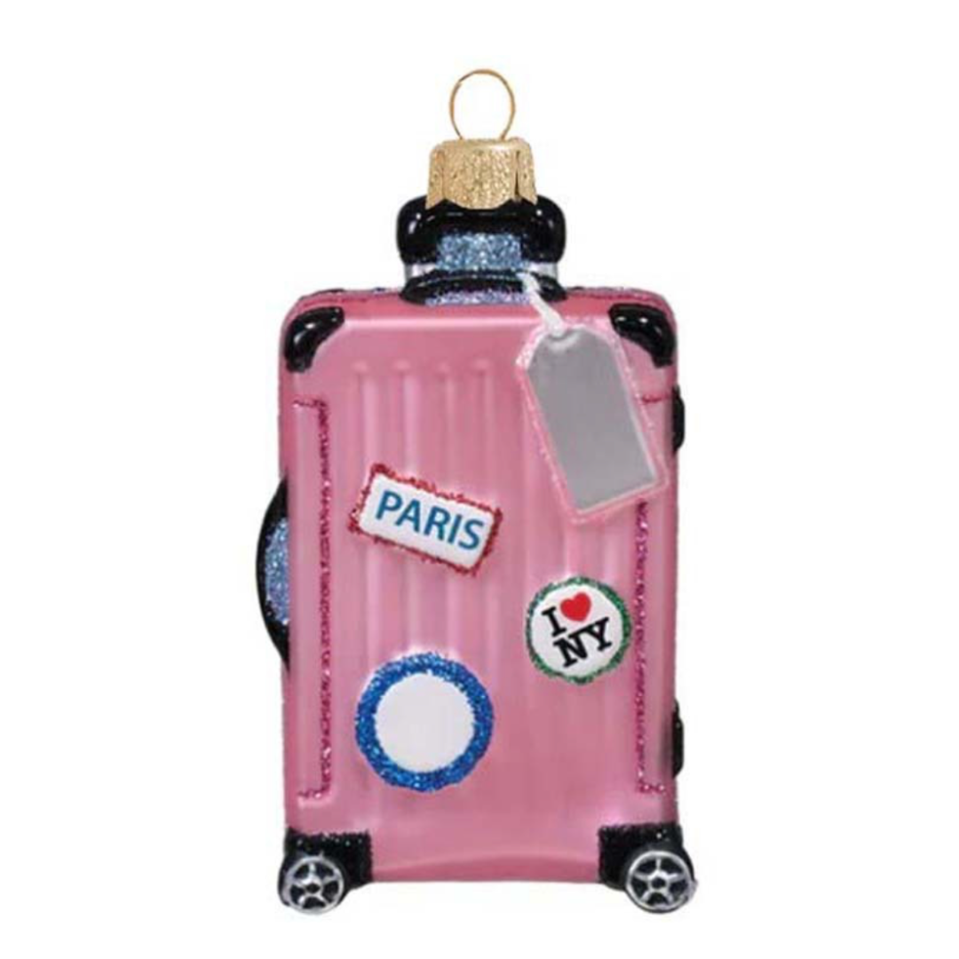 A pink suitcase-shaped Christmas ornament with glittery details, featuring travel-themed stickers that read PARIS and I <heart> NY, along with a hanging tag and a gold hanging loop.
